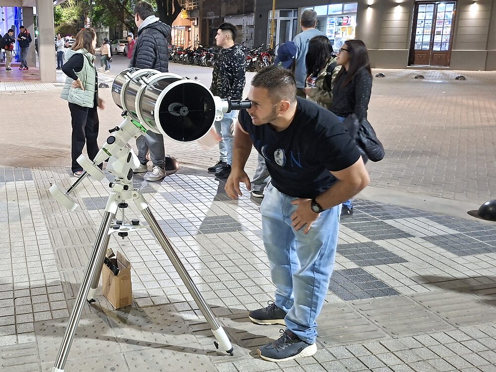 Una persona observa por un telescopio en la calle mientras otros esperan su turno